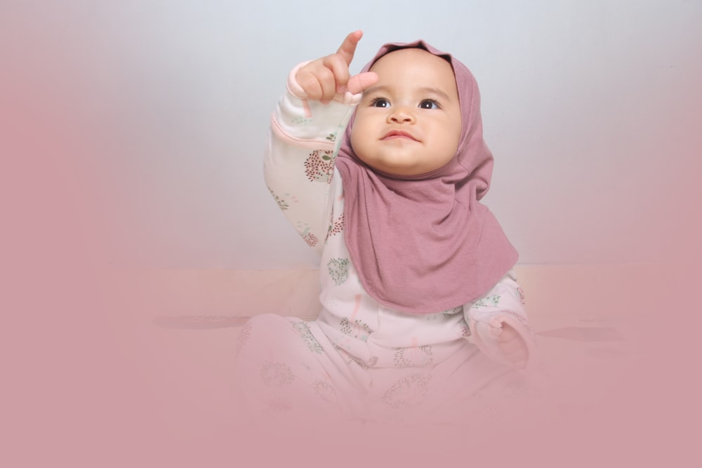 baby in white onesie lying on pink textile