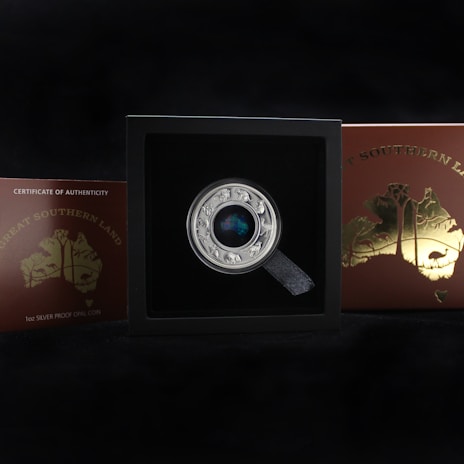 A collectible coin displayed in a black box with a label that reads 'Great Southern Land' and 'Certificate of Authenticity'. The coin has intricate designs with animals around the edge and a colorful central piece. The box and coin are set against a dark background.