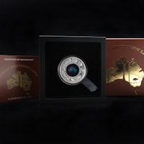 A collectible coin displayed in a black box with a label that reads 'Great Southern Land' and 'Certificate of Authenticity'. The coin has intricate designs with animals around the edge and a colorful central piece. The box and coin are set against a dark background.