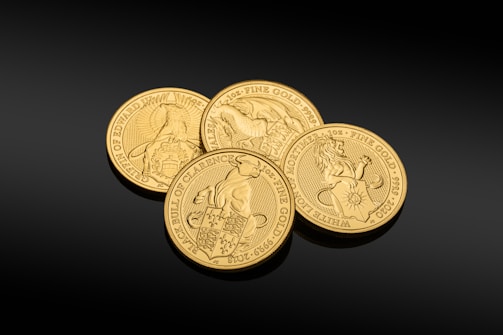 A set of gold coins with detailed engravings, each coin featuring different symbolic designs including animals and heraldic imagery. They are finely crafted and placed against a dark background, highlighting their luster and intricate artwork.
