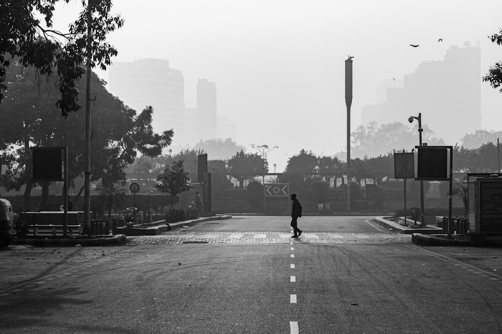 grayscale photo of man in black jacket and pants walking on sidewalk