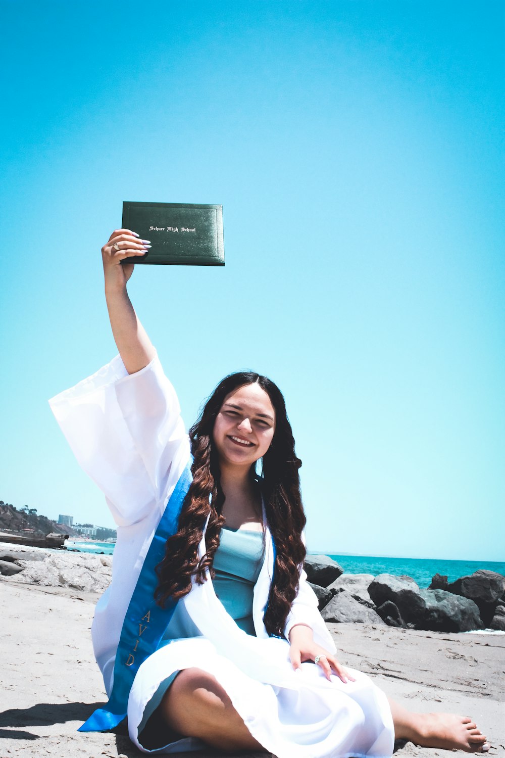 a woman sitting on the beach holding up a book