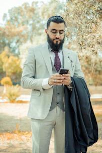 man in gray suit jacket holding black smartphone