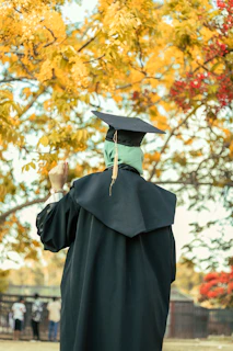 person in black academic dress holding brown leaves during daytime