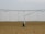 A large agricultural irrigation system is visible in a barren, flat field under an overcast sky. The system includes a long metallic structure with hoses hanging down from it, supported by a wheel.