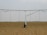 A large agricultural irrigation system is visible in a barren, flat field under an overcast sky. The system includes a long metallic structure with hoses hanging down from it, supported by a wheel.