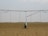 A large agricultural irrigation system is visible in a barren, flat field under an overcast sky. The system includes a long metallic structure with hoses hanging down from it, supported by a wheel.