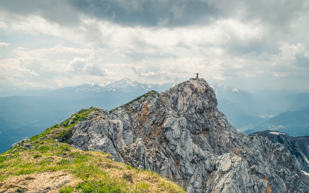 person standing on green grass field near gray rocky mountain under white clouds during daytime