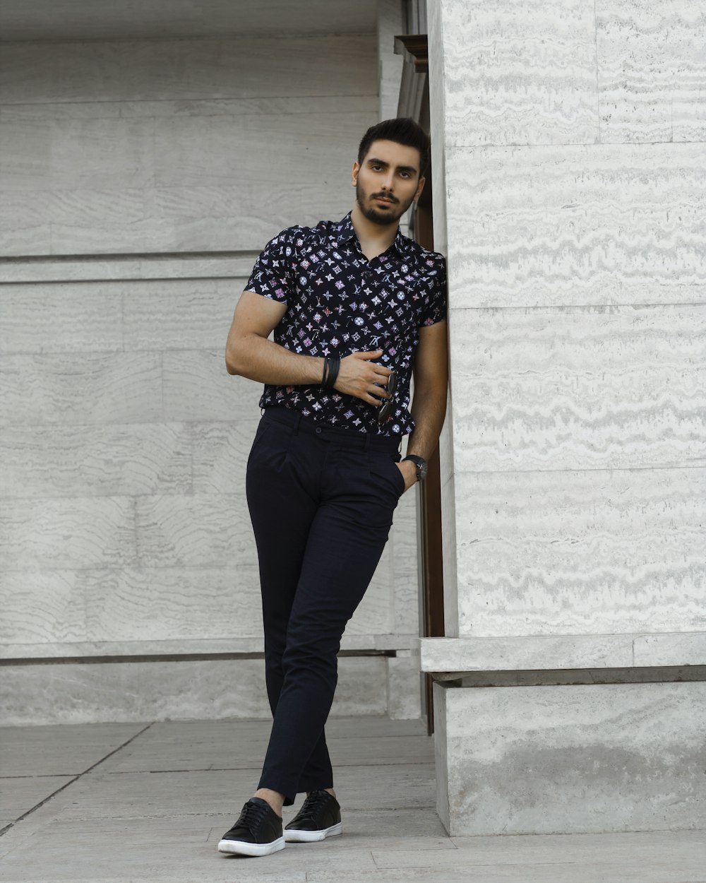 woman in black and white polka dot shirt and black pants standing beside white wall