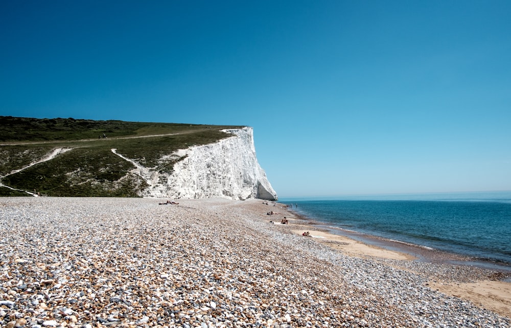 gray rocky mountain beside blue sea under blue sky during daytime