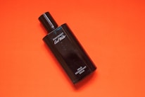 A black bottle of Davidoff Cool Water deodorant rests against a vibrant orange background. The bottle is sleek, with white text labeling it as mild deodorant. The contrast between the dark bottle and the bright background creates a striking visual.