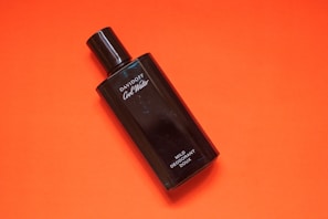 A black bottle of Davidoff Cool Water deodorant rests against a vibrant orange background. The bottle is sleek, with white text labeling it as mild deodorant. The contrast between the dark bottle and the bright background creates a striking visual.