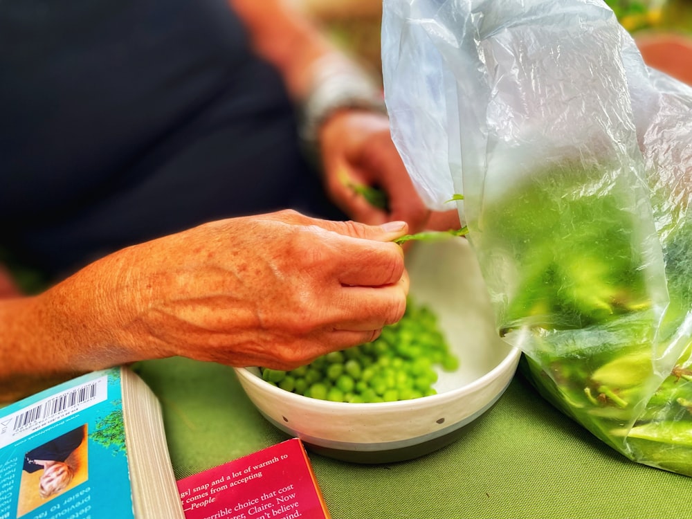 person holding green vegetable in white plastic bag