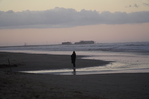 person in black coat walking on beach during daytime