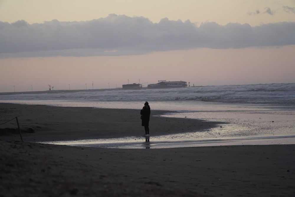 Persona con abrigo negro caminando por la playa durante el día