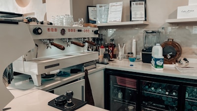 Cozy coffee bar area with cups, coffee machine, and fridge in the background.