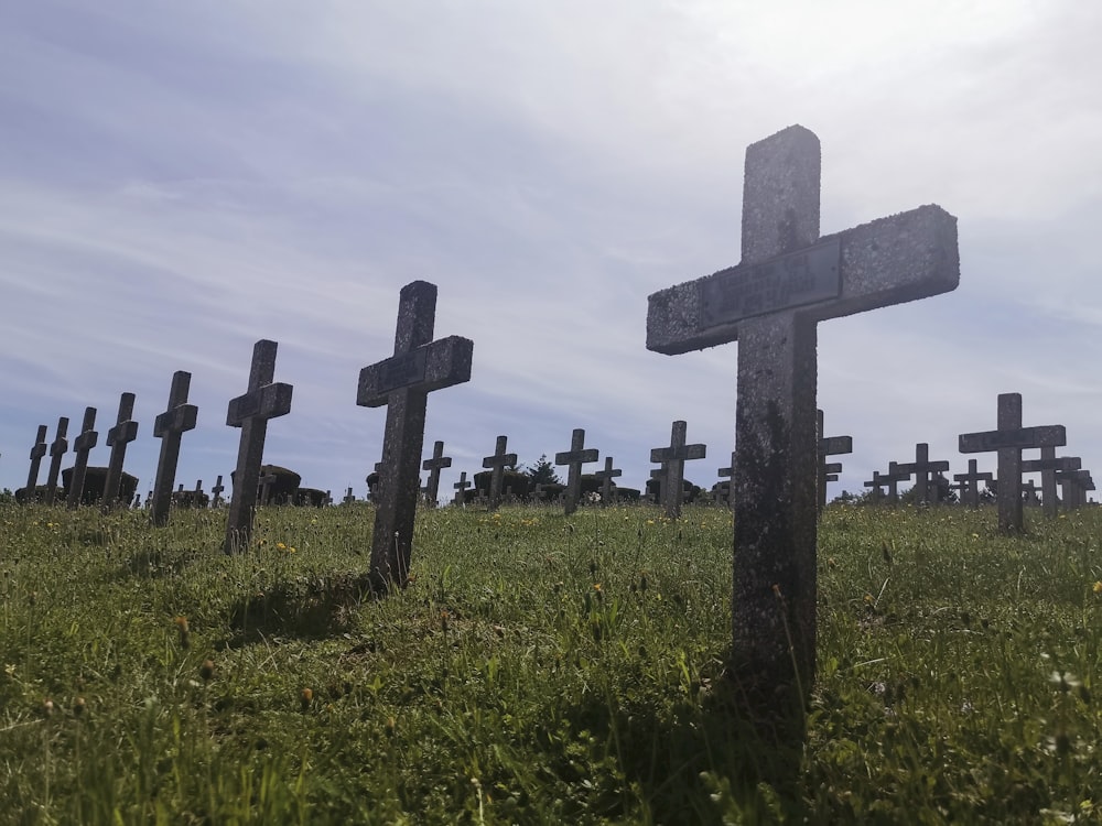 Croix grise sur un champ d’herbe verte sous des nuages blancs pendant la journée