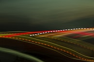 Streaks of colorful light trails move across a dark background, producing an abstract and dynamic visual effect. The trails include red, yellow, orange, and white colors.