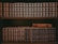 A bookshelf filled with dark-colored volumes, primarily containing the works of Honoré de Balzac, is arranged neatly on the shelves. The upper shelf features a complete series of La Comédie Humaine, with uniform covers and gold lettering. The lower shelf holds books by Guy de Maupassant, along with an old, ornate hardcover book placed on top.