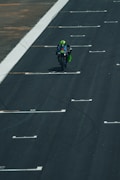 A motorcyclist is riding a racing motorcycle on a track. The rider is wearing a green and black racing suit and helmet, and the motorcycle has the number 46 prominently displayed. The track is marked with white lines and appears to be an asphalt surface.