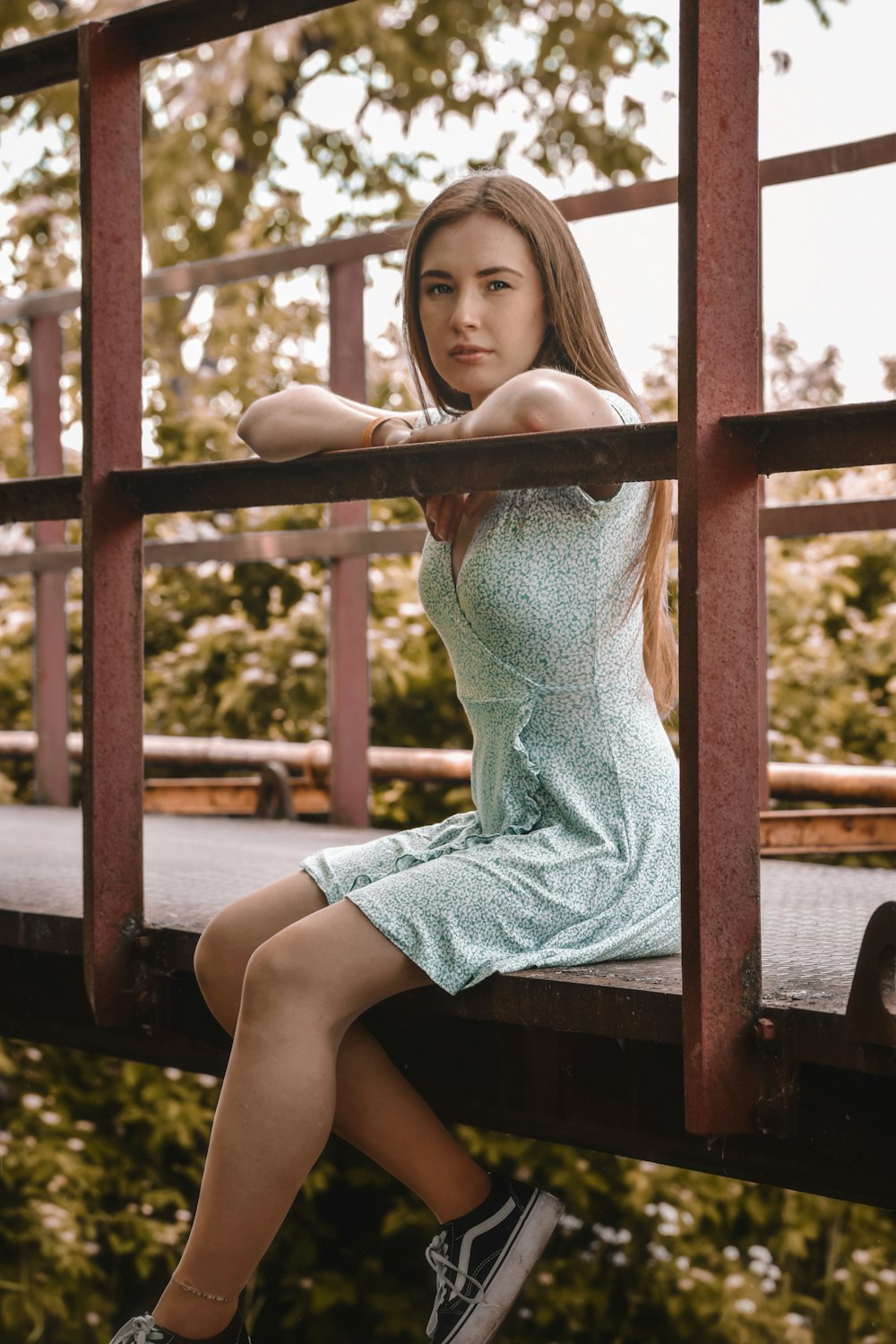 girl in blue dress sitting on brown wooden fence during daytime