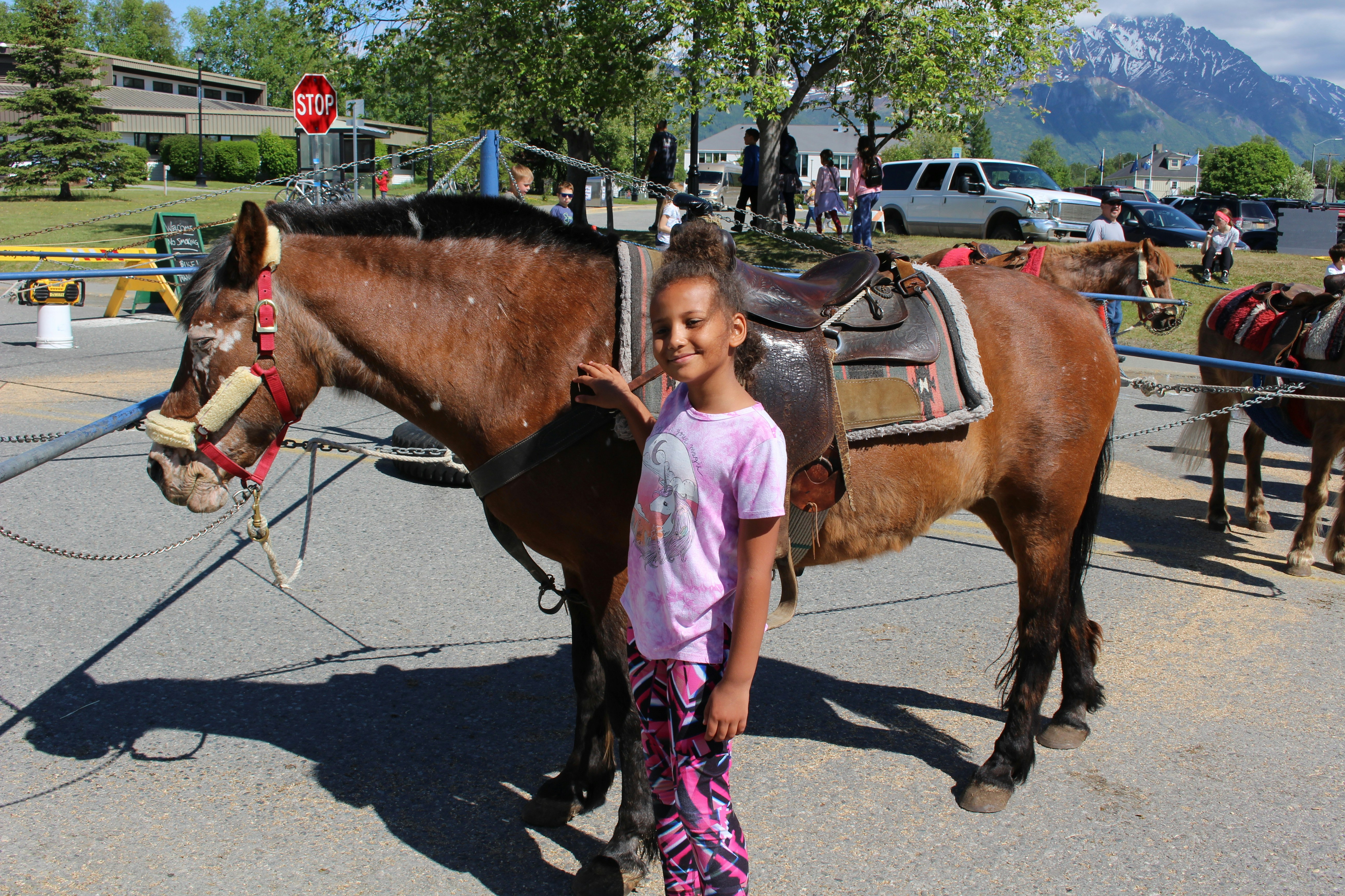 A young rider adjusting her stirrups while smiling beside her horse in a sunny paddock