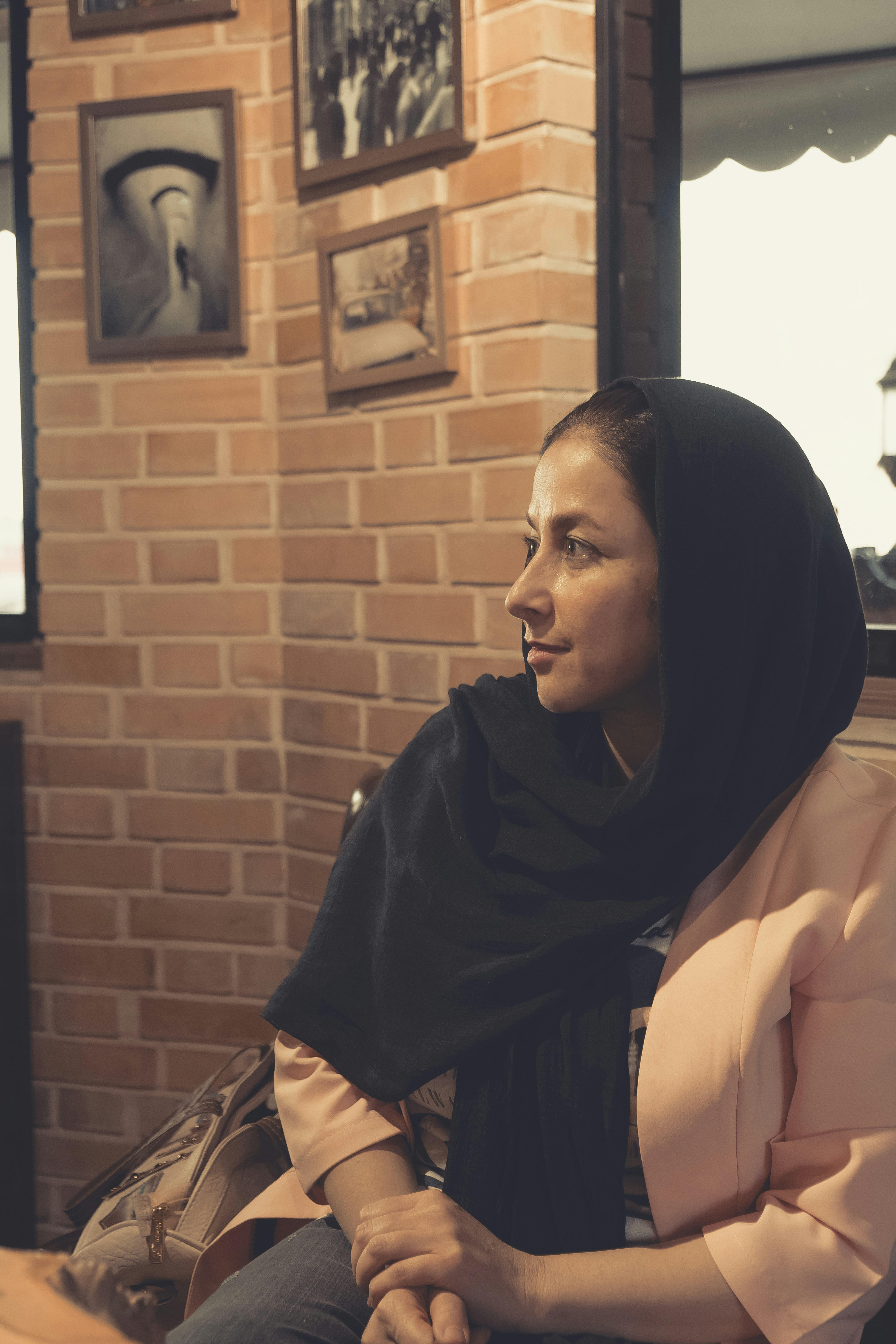 Wanita berjilbab hitam duduk di samping dinding bata coklat