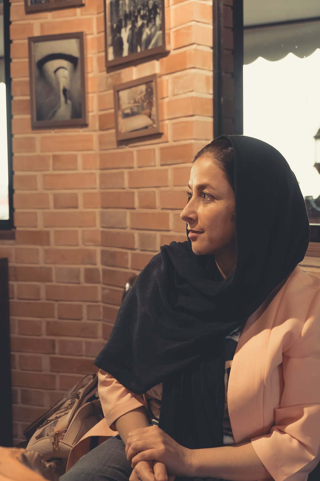woman in black hijab sitting beside brown brick wall