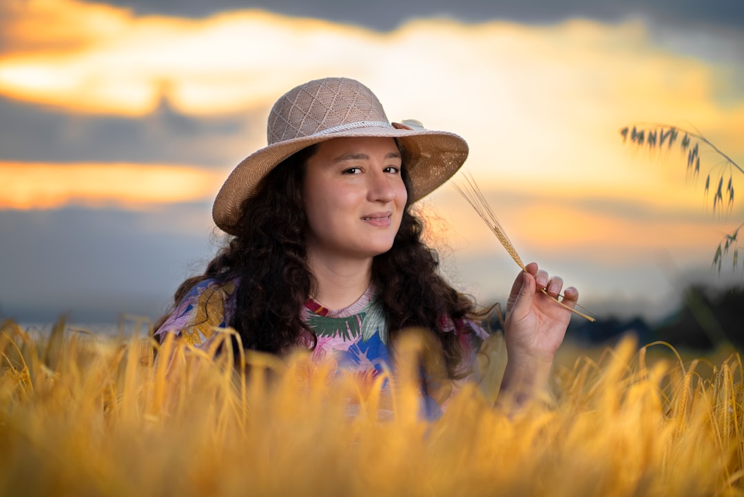 woman in blue and yellow tie dye shirt wearing brown hat standing on yellow flower field