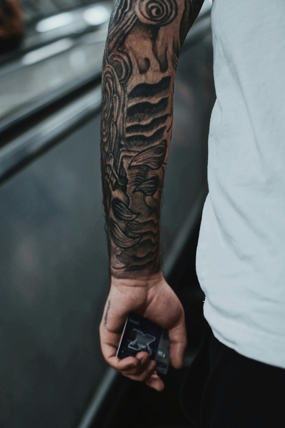 person with black tattoo holding black smartphone