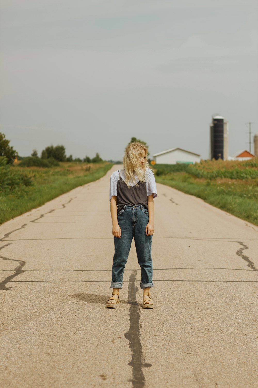 흰색 티셔츠와 파란색 데님 청바지를 입은 여자가 낮에 회색 콘크리트 도로를 걷고 있다