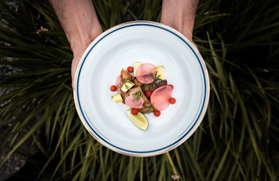 Close-up of hands styling a plate with fresh herbs and ripe ingredients for a social media shoot.