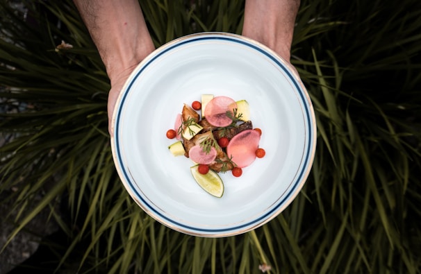 Hands plating a vibrant dish with various fresh vegetables.