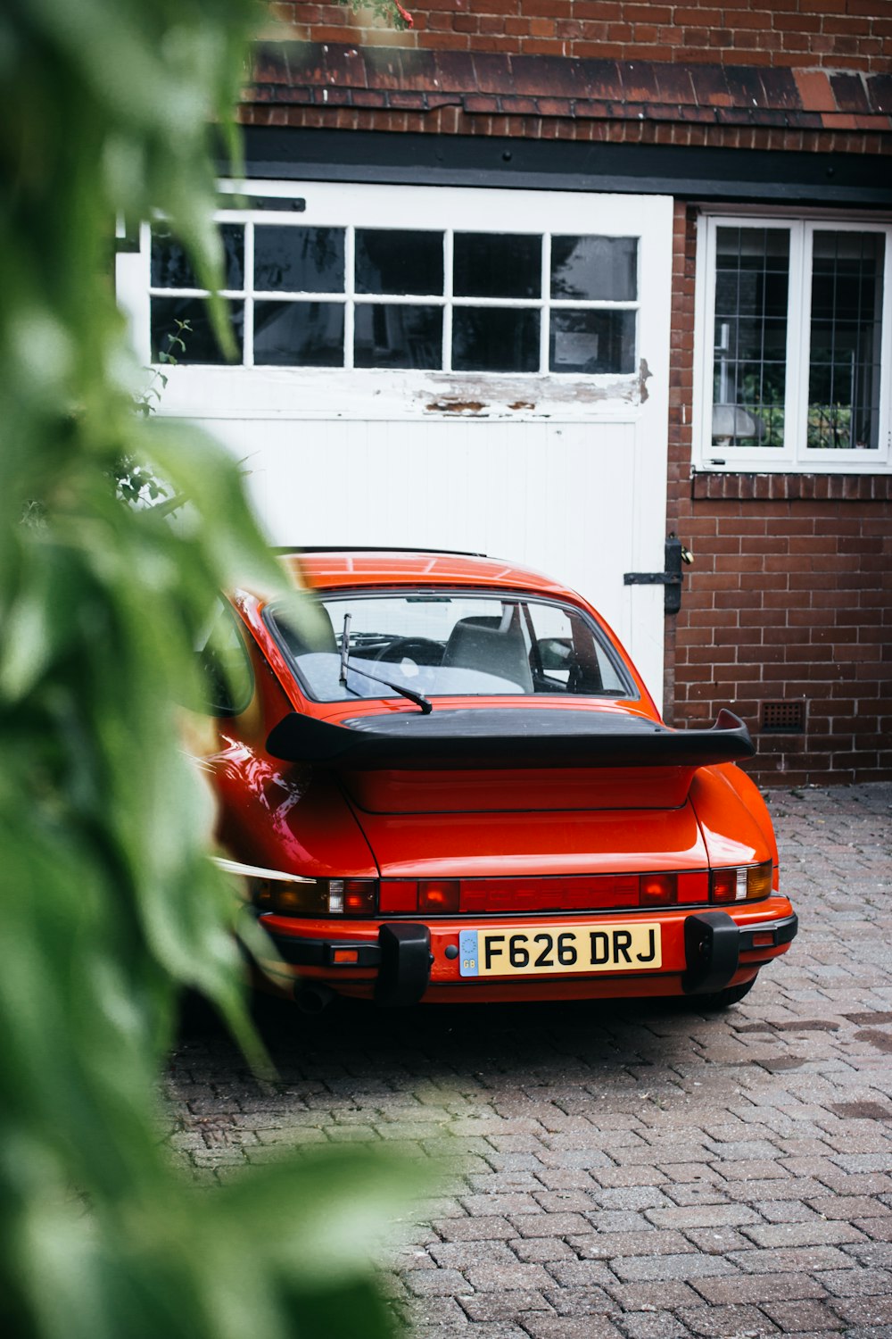 red porsche 911 parked beside green leaf plant