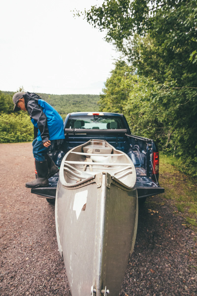 A person loading a grey canoe into the back of a pickup truck on a country lane