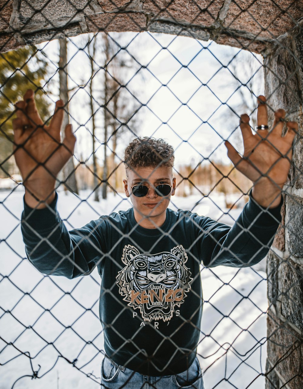 a man wearing sunglasses behind a chain link fence
