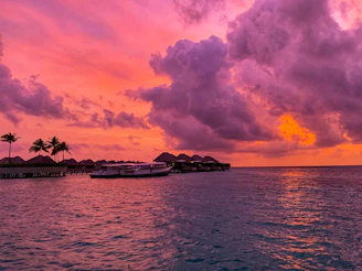 A vibrant tropical ocean scene with crystal-clear turquoise waters, a traditional Maldivian boat, and a sunset casting warm golden hues over the horizon.