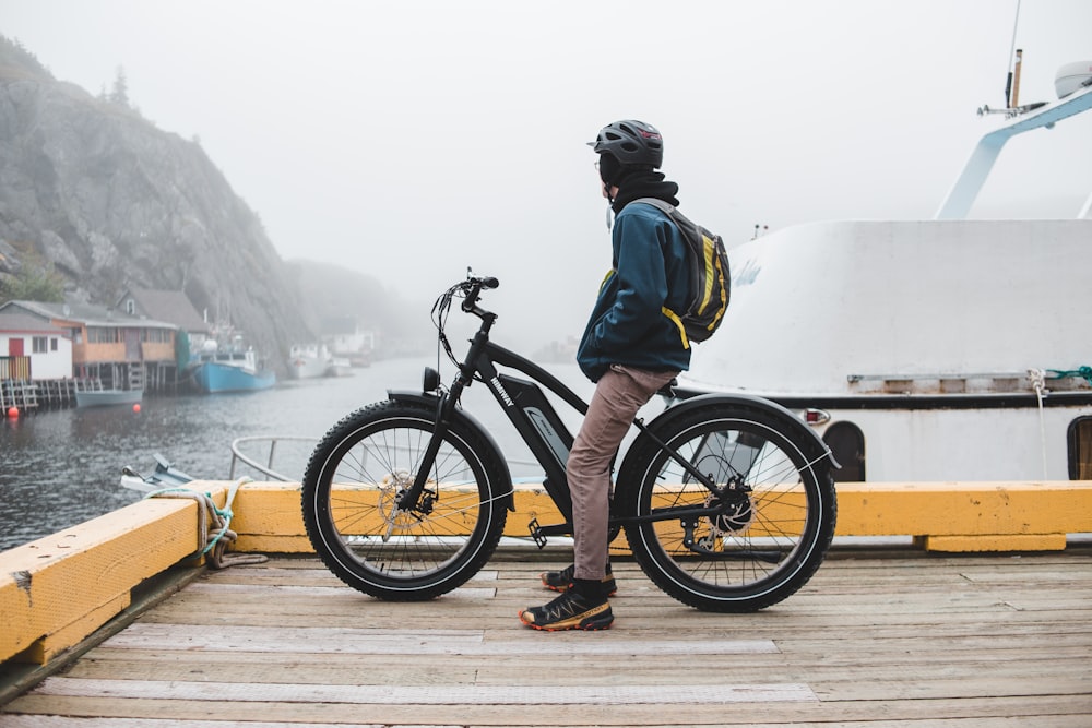 Hombre en chaqueta verde montando bicicleta negra en muelle de madera marrón durante el día