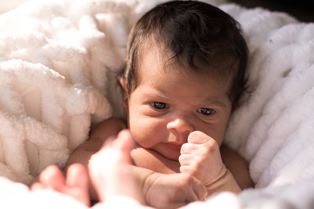 baby lying on white fur textile