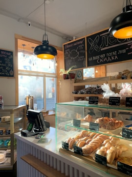 A cozy bakery with a variety of breads and pastries displayed in a glass case. The interior features wooden accents, chalkboard menus, and hanging pendant lights. Sunlight streams through large windows, creating a warm and inviting atmosphere.