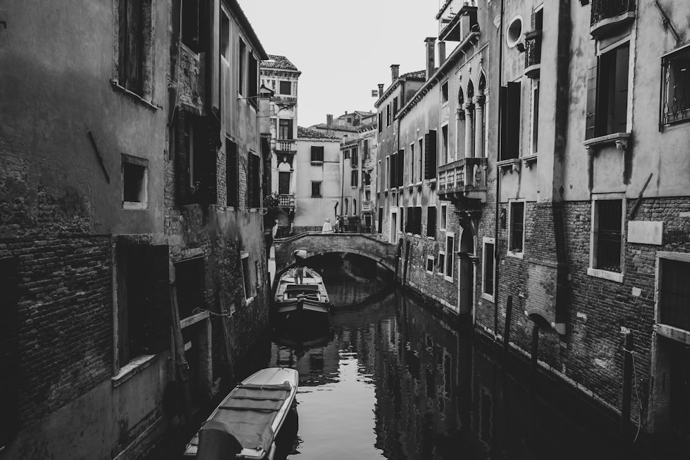 grayscale photo of river between concrete buildings