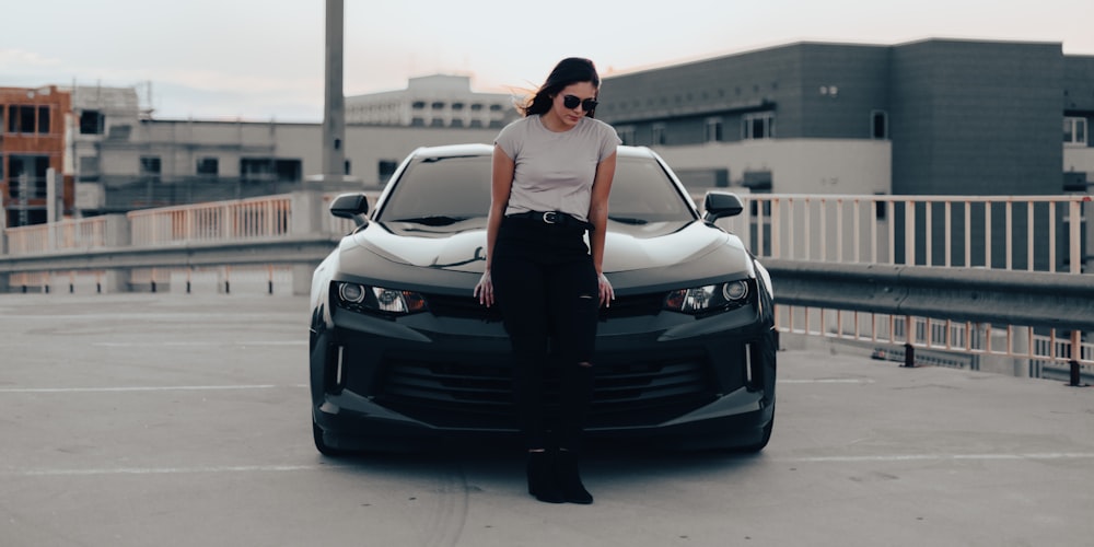 woman in white tank top and black skirt leaning on black car