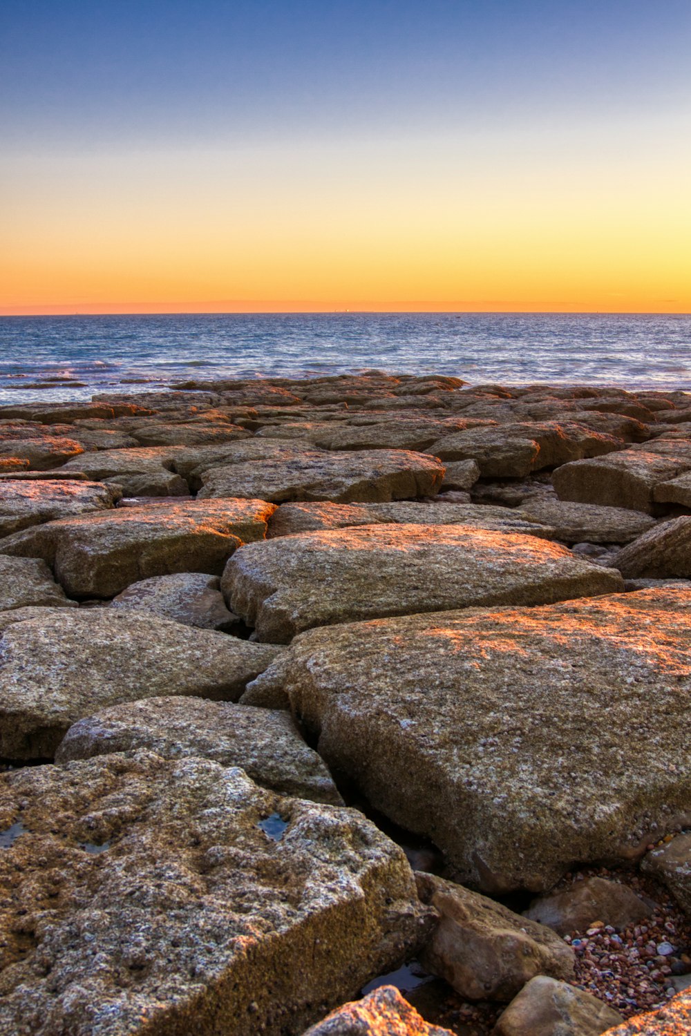 the sun is setting over a rocky beach