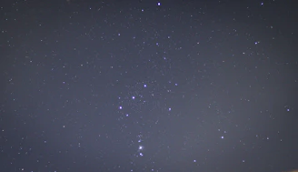 A serene night sky with the Orion constellation shining brightly above a calm city skyline.
