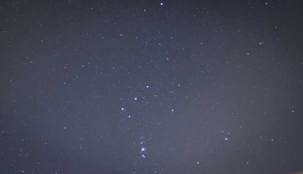 A serene night sky with the Orion constellation shining brightly above a calm city skyline.