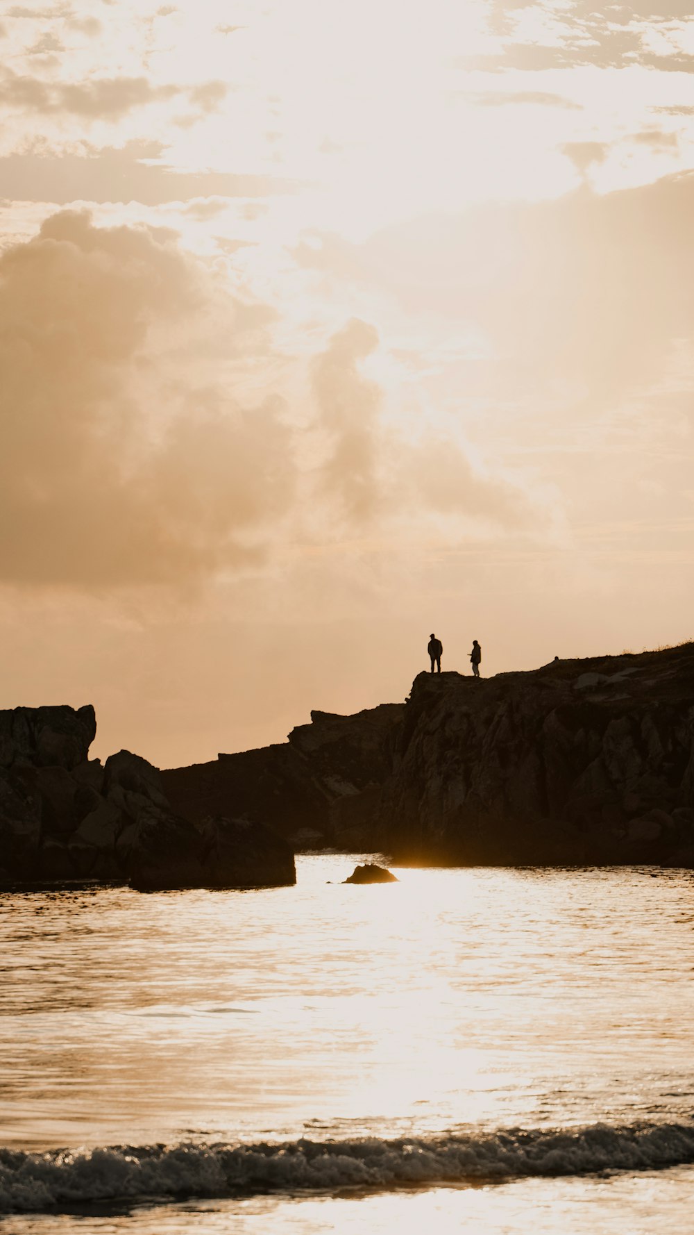 silhouette of 2 people standing on rock formation near sea during daytime
