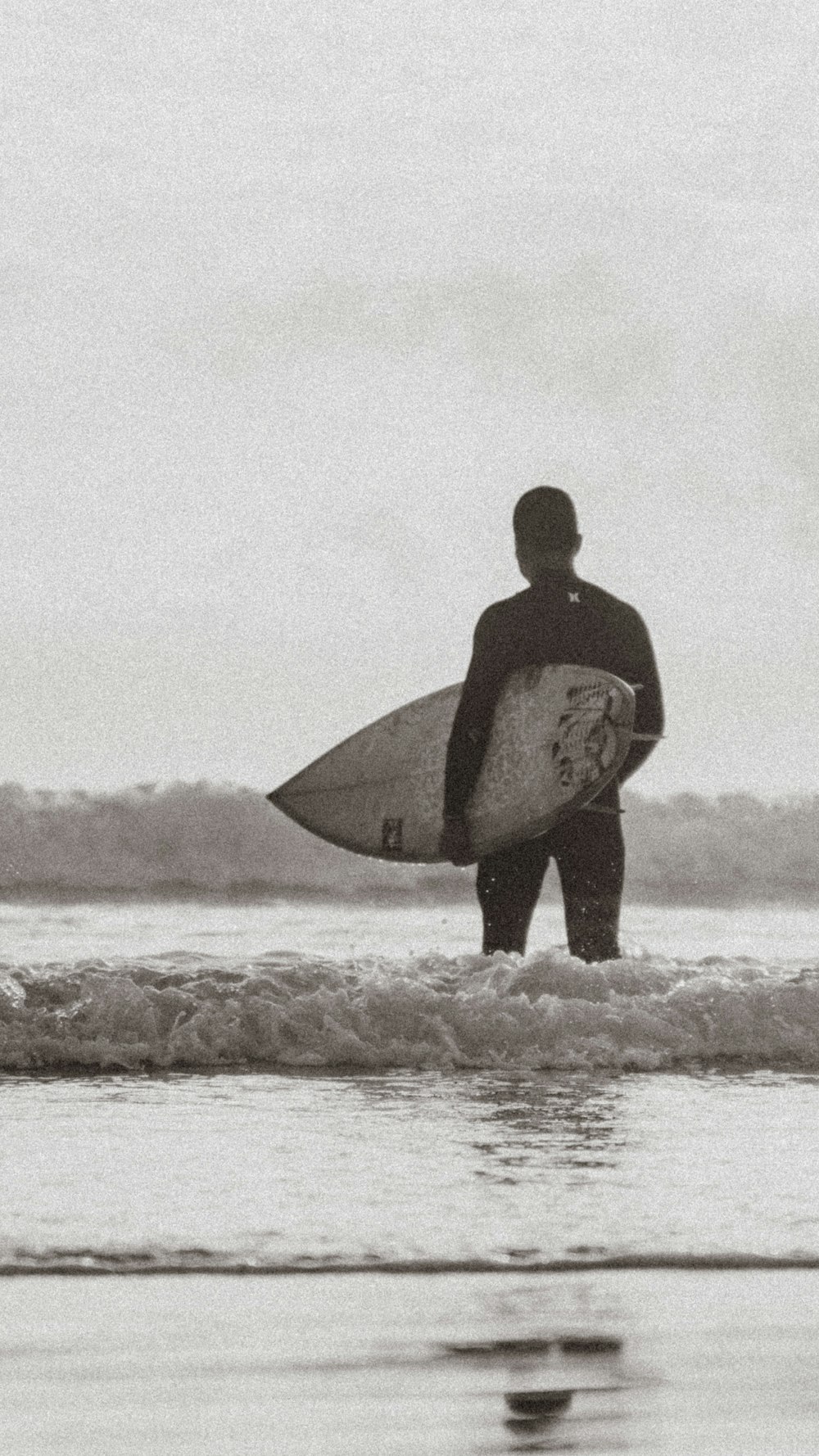 man in black wet suit holding surfboard on beach