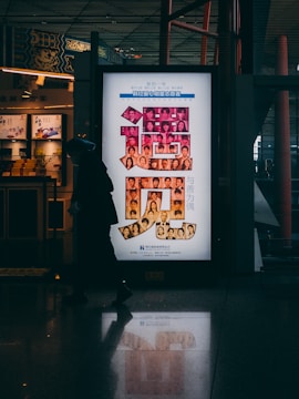 man in black jacket standing near white and red poster
