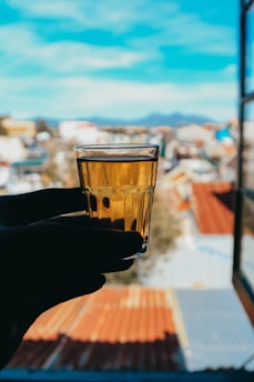 Hands holding a finished glass tumbler with city skyline blurred in background.