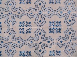 Intricate ceramic tiles with blue floral and geometric patterns on a beige background, showcasing a repeating symmetrical design.